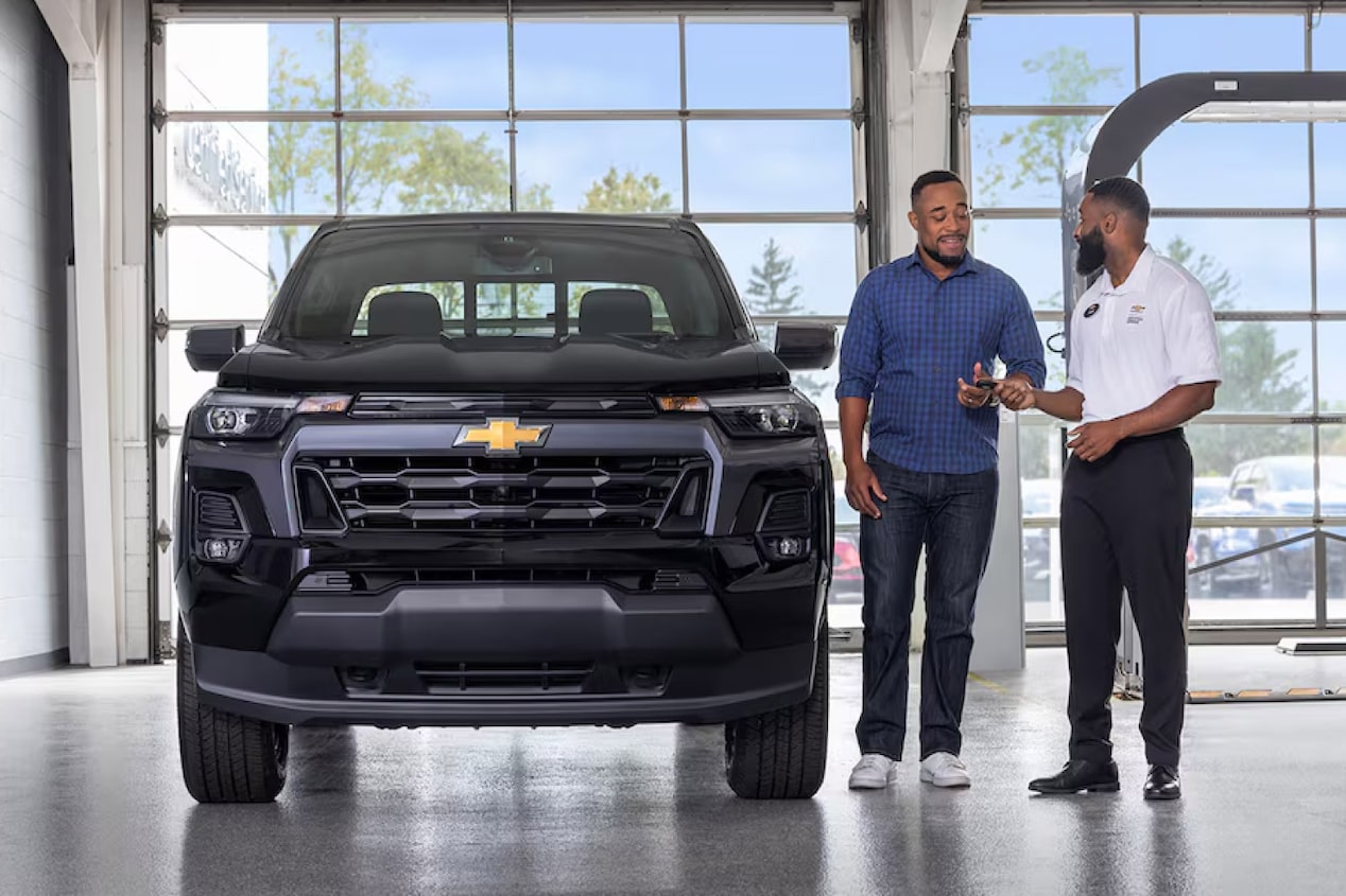 Front View of a Chevy Vehicle with a Dealer Handing Out the Key to the Owner