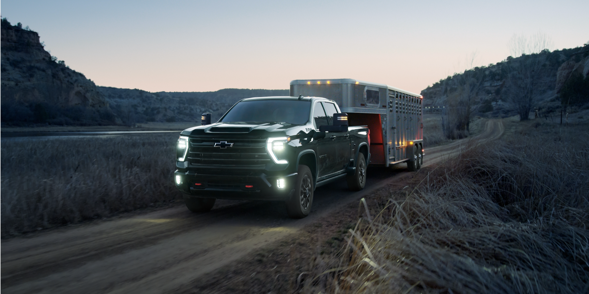 Silverado HD Trail Boss Towing an Animal Trailer Down a Highway at Dusk