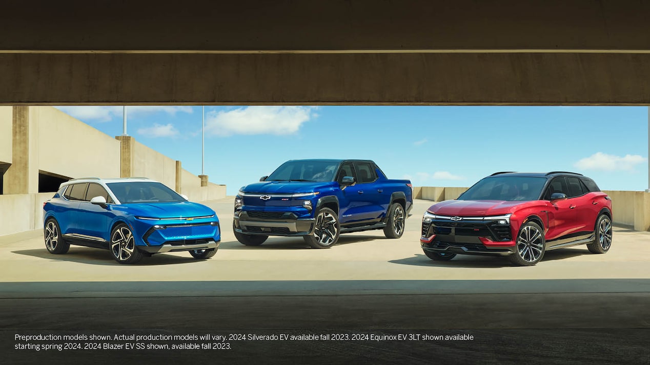 A blue Equinox EV, a blue Silverado EV, and a red Blazer EV are parked together on the open top level of a parking garage.