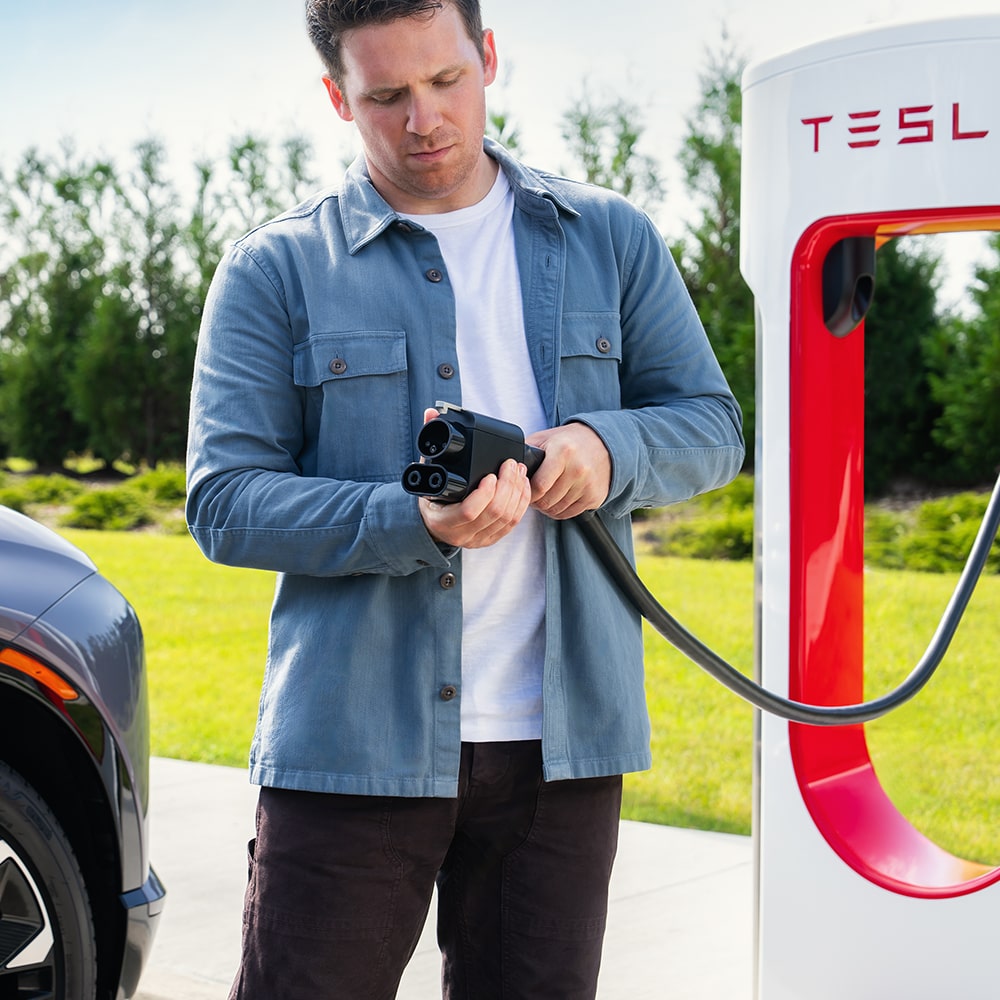 A Man Using a Public Tesla EV Charger to Charge His Chevy EV