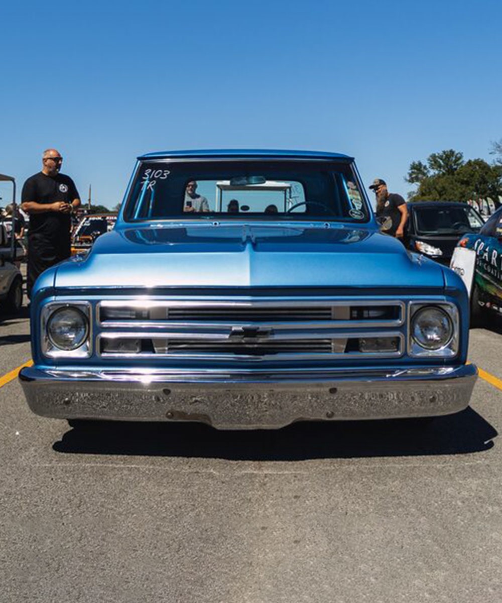 Vista delantera de pickup Chevy azul clásica en excelente estado con un hombre parado cerca de la caja