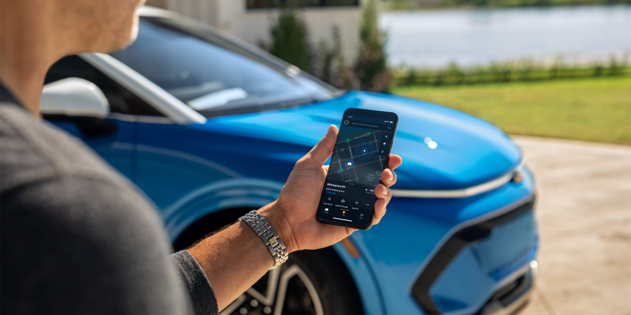 A Man Using the myChevrolet App on iPhone with Blue Equinox EV in Background