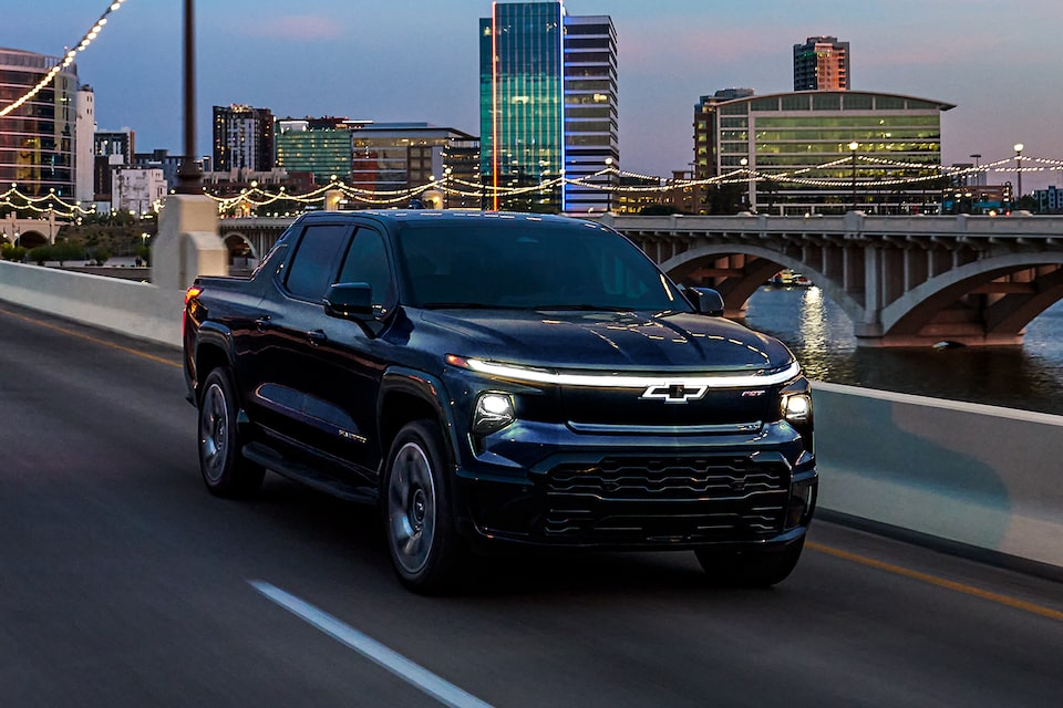 Vista de tres cuartos de una Chevrolet Silverado EV 2025 negra circulando por una carretera de noche.