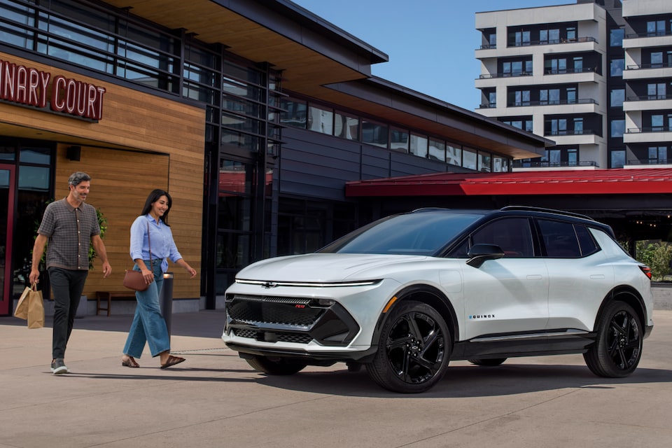 Una mujer y un hombre acerándose a una Chevrolet Equinox EV 2025 blanca después de hacer compras