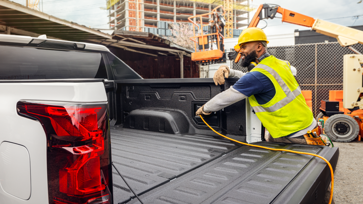 A Construction Worker Plugging in an Extension Cord in the Bed of a Silverado EV