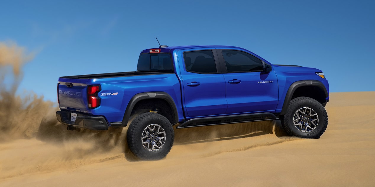 Three Quarters Rear View of a 2025 Blue Chevy Colorado Driving Upward on a Desert